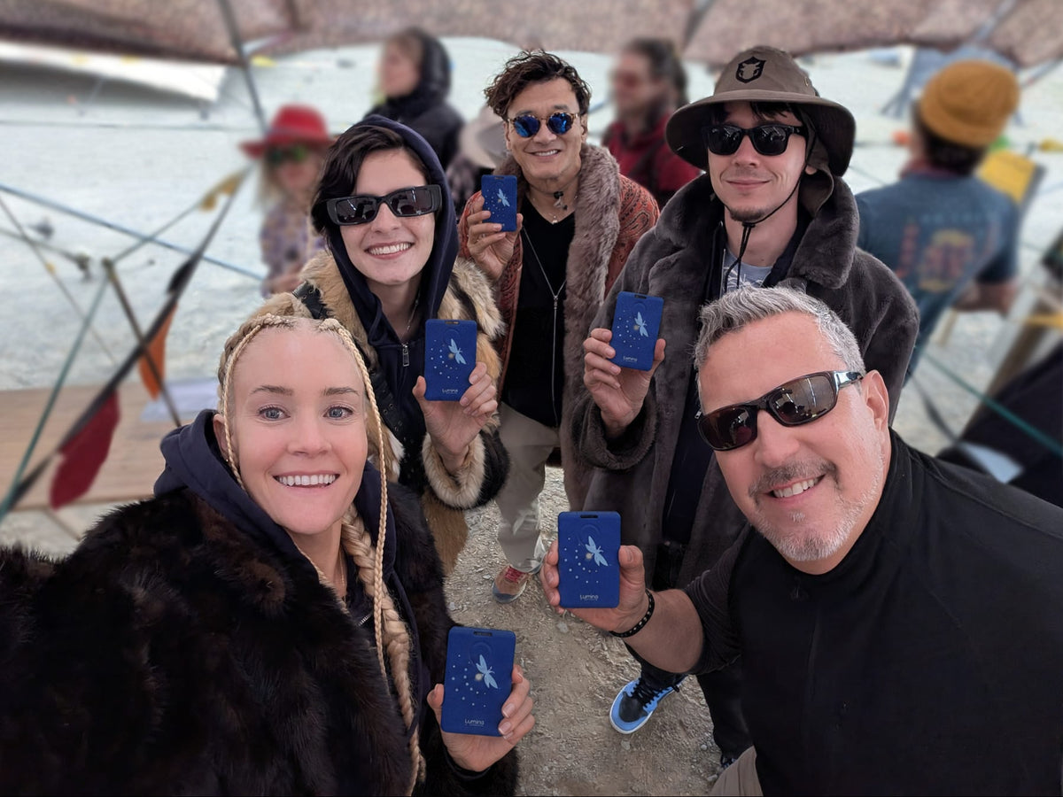 Group of five people at an outdoor festival, each holding a blue Lumina device.