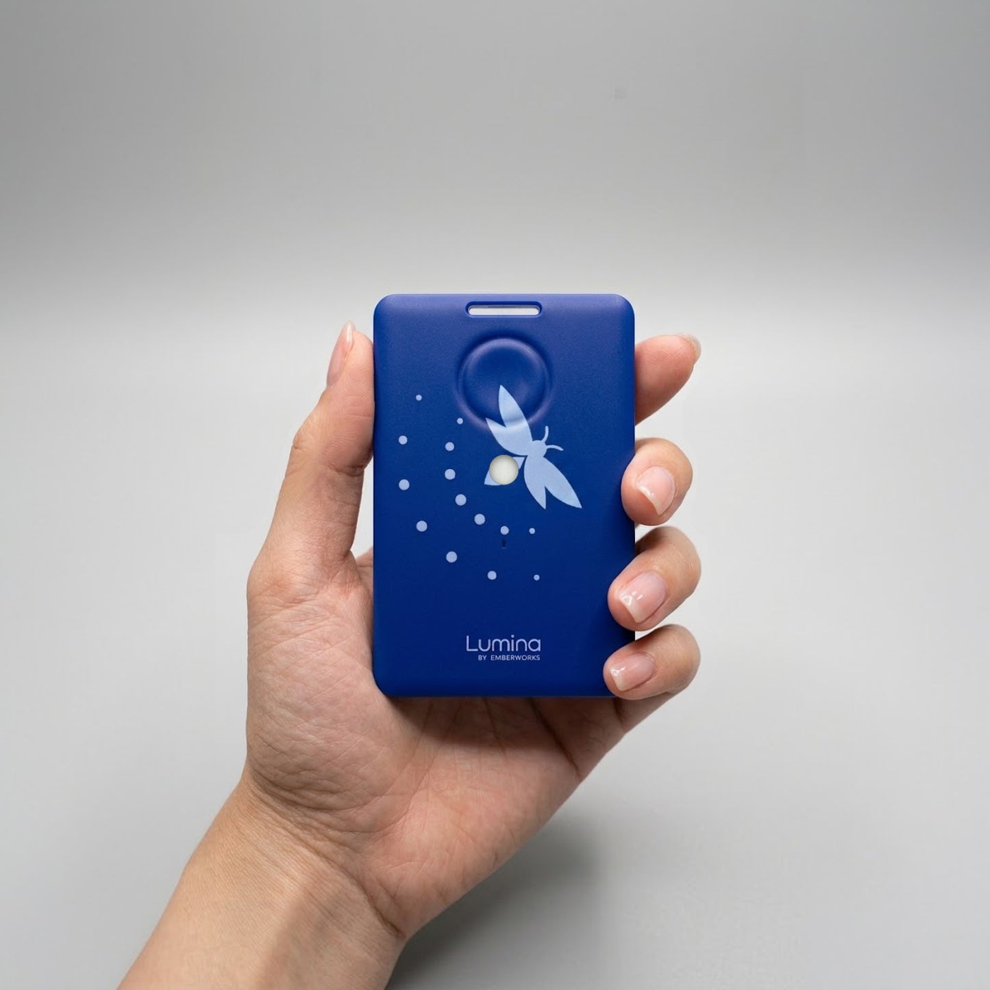 Hand holding a blue Lumina device with a firefly design on a gray background.