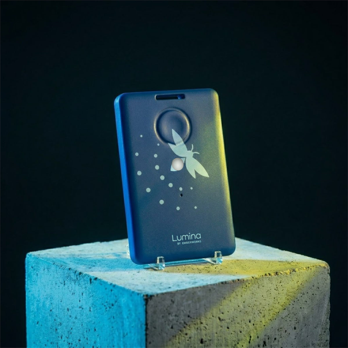 Blue device with 'Lumina by EmberWorks' branding on a concrete block against a dark background